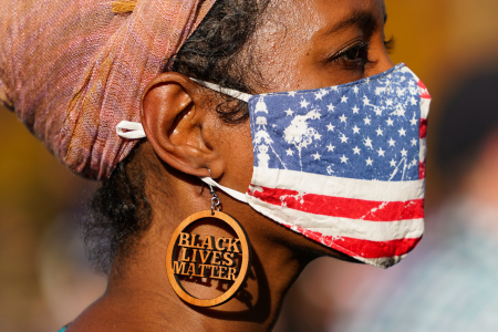 A woman wearing Black Lives Matter earrings and an American flag mask watches the celebrations of Joe Biden's election victory at Independence Mall in Philadelphia, Pa. on Nov. 7, 2020.