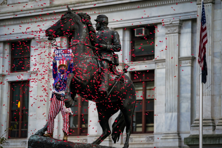 A man dressed as Uncle Sam climbs on the statue of General George McClellan outside the City Hall building, throwing red confetti and holding up a Biden-Harris sign in Philadelphia, Pa. on Nov. 7, 2020.