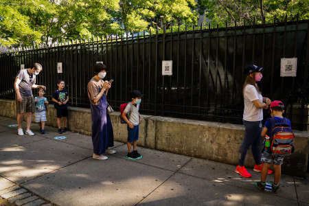 Campers and parents line up, masked and socially distanced, outside the entrance gate before the first day of camp on June 29, 2020. Parents were required to check in their children and complete a health screening for them each day using QR codes taped to the gate before entering the campus.