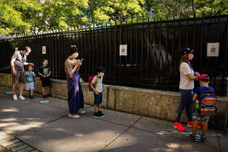 Campers and parents line up, masked and socially distanced, outside the entrance gate before the first day of camp on June 29, 2020. Parents were required to check in their children and complete a health screening for them each day using QR codes taped to the gate before entering the campus.