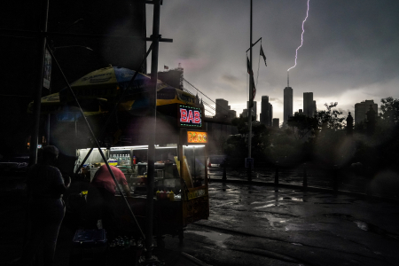 A man cooks at his halal food cart as lightning strikes One World Trade Center during a thunderstorm in New York, N.Y. on June 4, 2021.