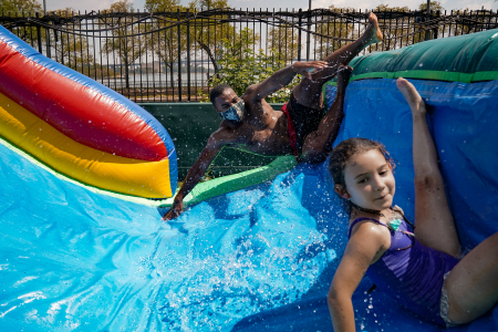 Patrick Lindo, a counselor in the seven to eight-year-old division, rides down a water slide with a camper on Aug. 10, 2020. Counselors were required to wear masks during water activities, but campers were not.